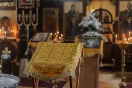 Anonymous hands in prayer pose before a simple home altar with oil lamp and flowers in morning light