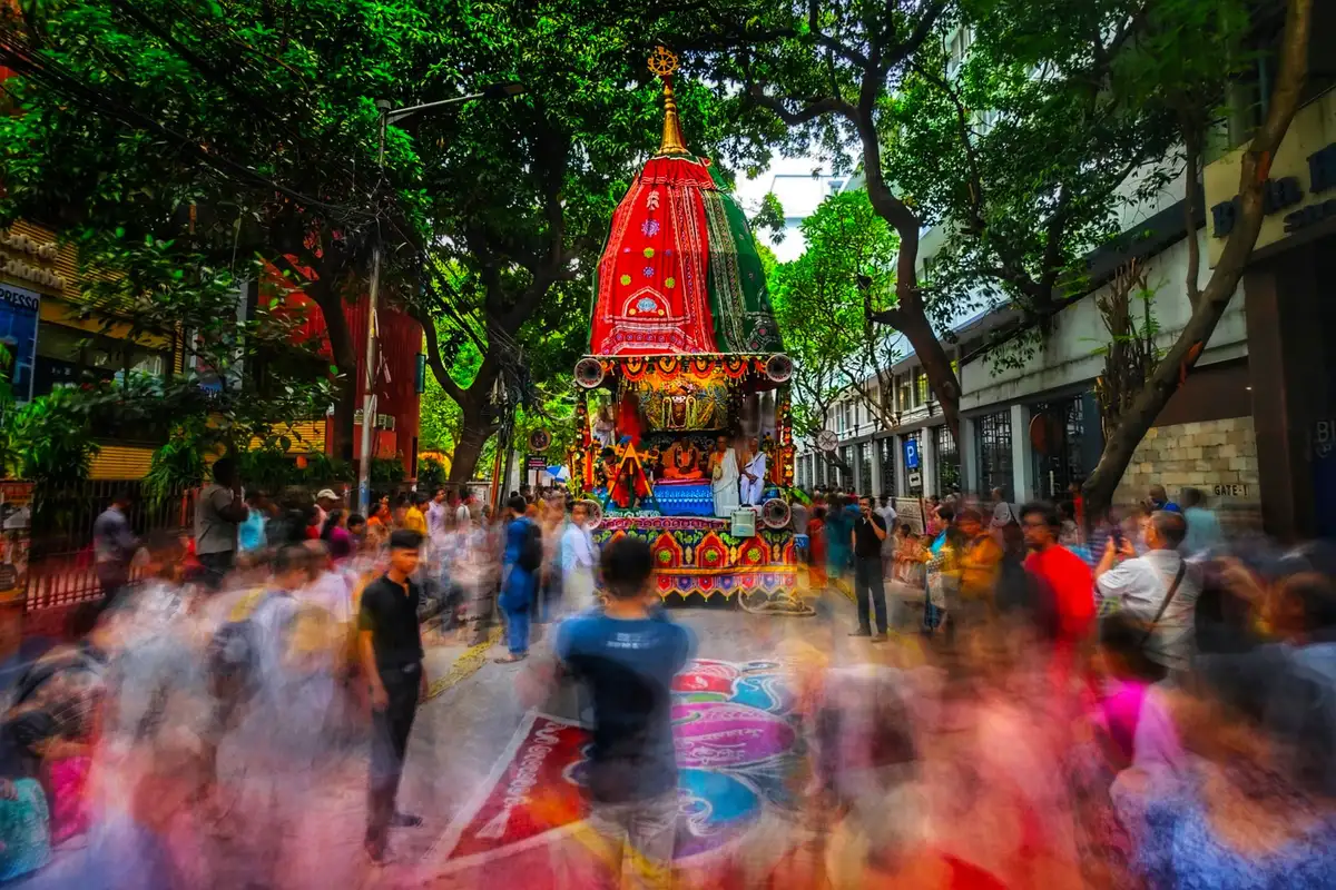 Devotees pulling ropes attached to a massive wooden chariot decorated with colorful fabric during the Rath Yatra process