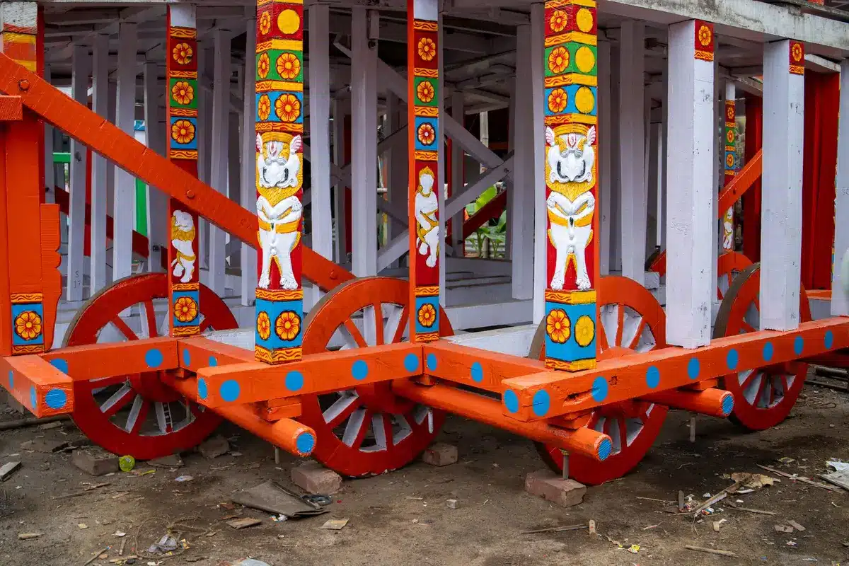 Master craftspeople working on intricate wooden chariot construction using traditional tools and techniques
