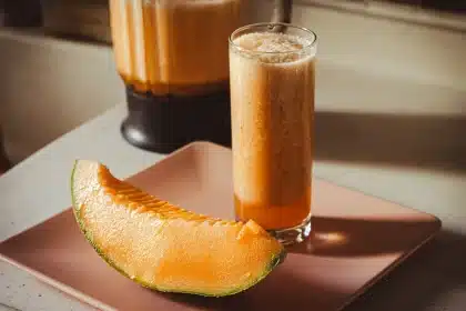 Warm sweet potato smoothie being poured into a bowl with steam rising, surrounded by fresh ingredients and spices.