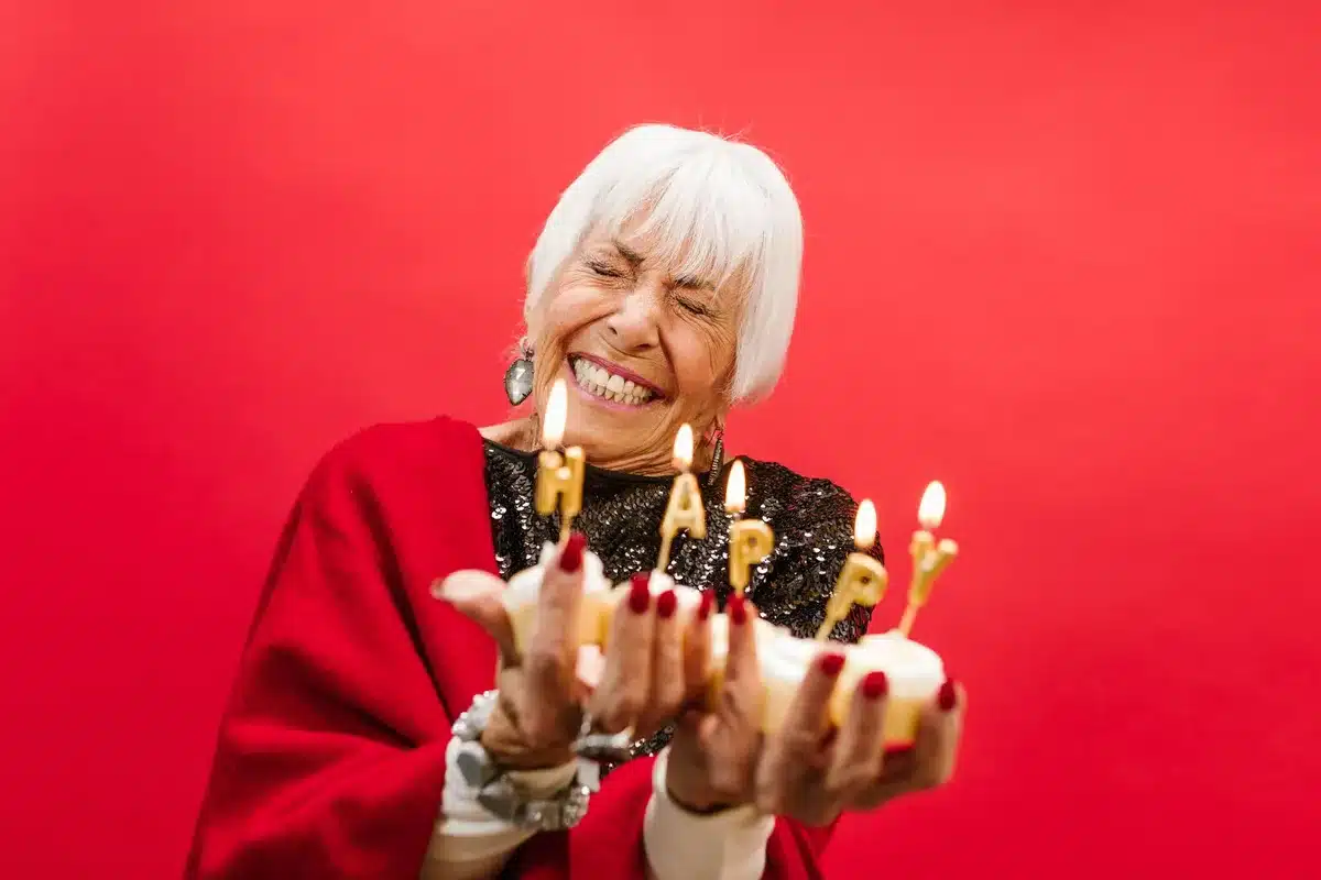 An elder woman receiving respectful gestures during a birthday celebration, surrounded by warm lighting and traditional