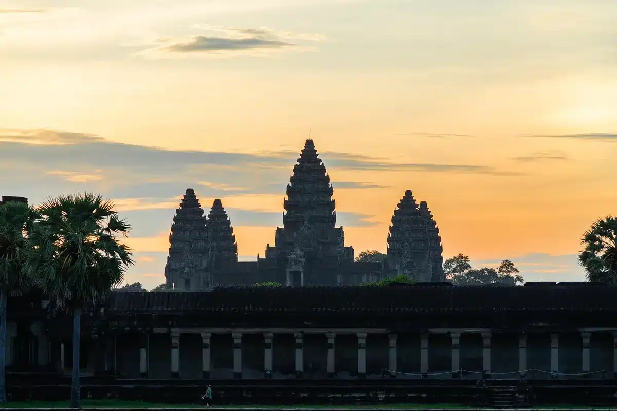 Pilgrims walking toward ancient Buddhist temple at sunrise with spiritual monuments in background