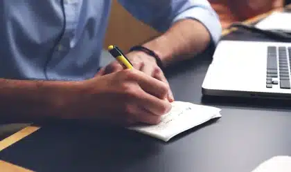 Hands holding meditation beads above a notebook and laptop on a table in a community hall