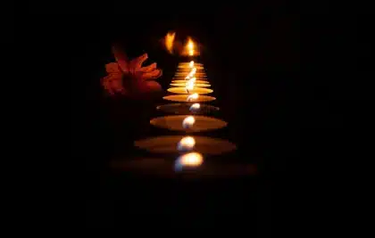 Riverside ghats lit by rows of oil lamps with silhouetted figures at dusk
