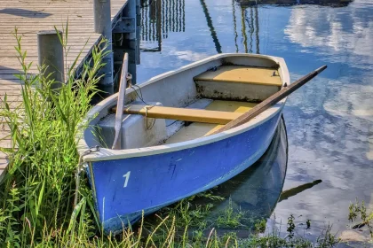 Abandoned shoes and prayer beads on a riverbank beside a small boat at sunrise