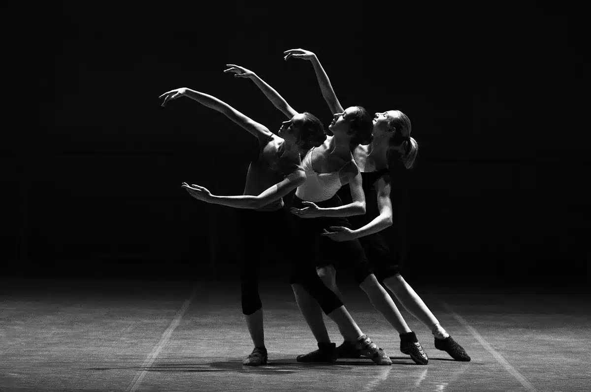 Silhouetted young classical dancers rehearsing on a wooden stage with empty auditorium