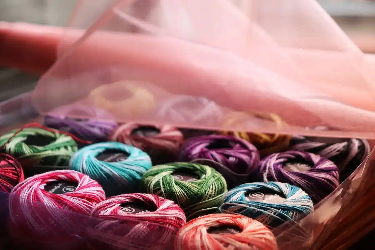 Anonymous hands stitching metal-thread zardozi embroidery on fabric with silk thread spools