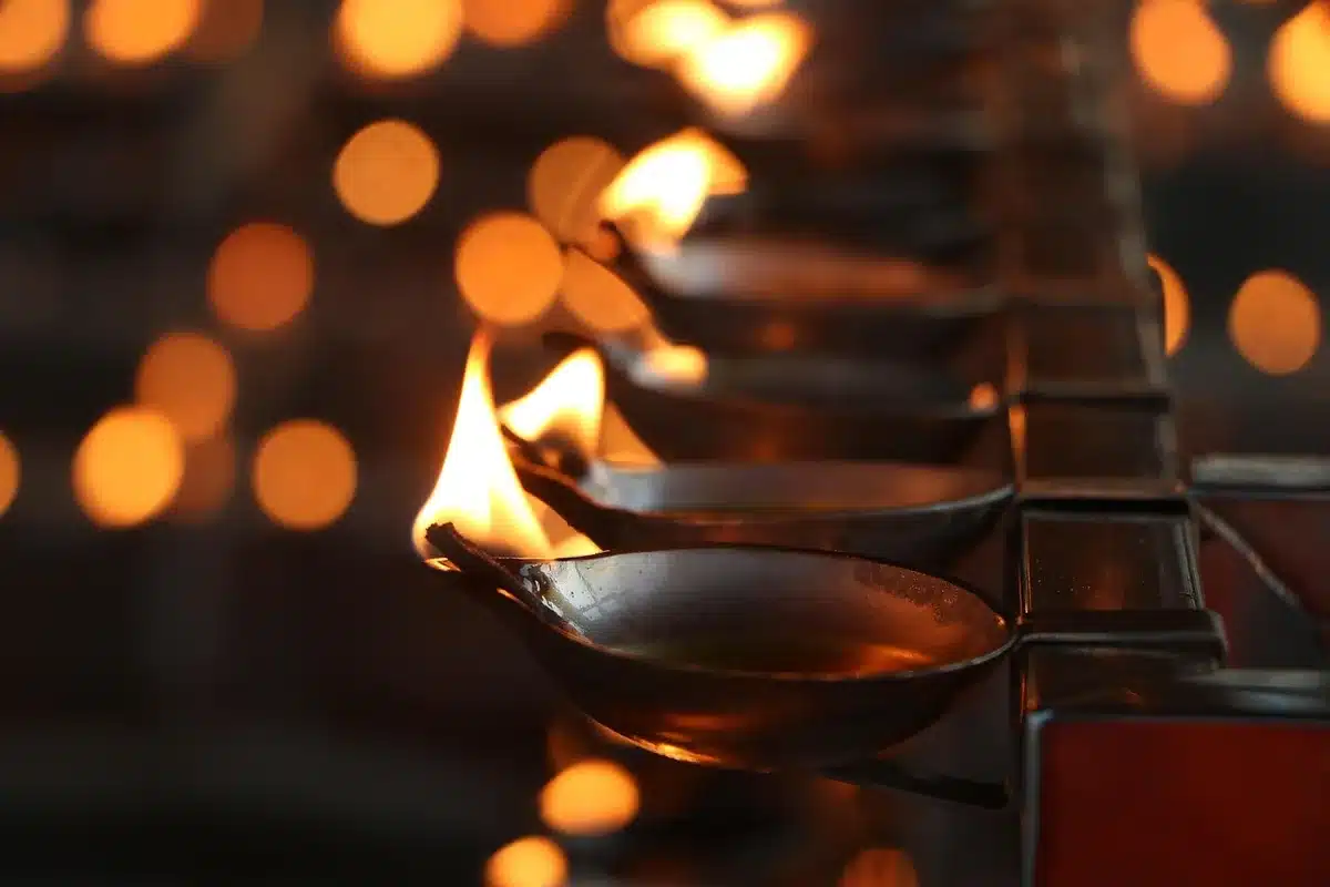 Bowl of kheer covered with muslin beside a lit oil lamp on a courtyard table at dusk